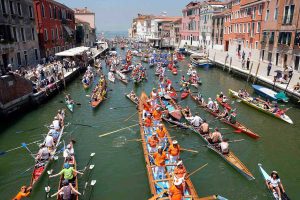 viele bunte Drachenboote mit pinken Paddlerinnen schwimmen in einem Lanal in Venedig